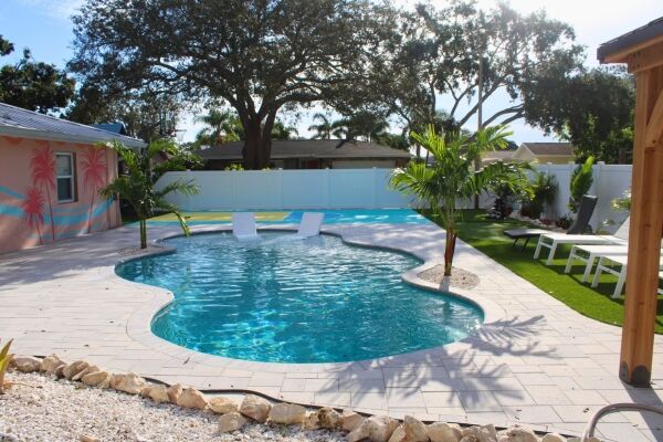 Residential backyard swimming pool with tropical landscaping, lounge chairs, and clean blue water, showcasing a professionally maintained pool service outdoor living space.