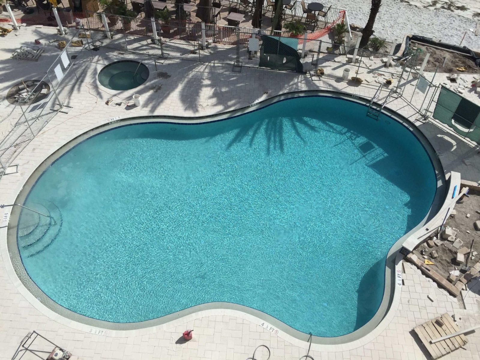 Aerial view of freeform resort-style swimming pool with light stone paver deck and spa area during renovation.