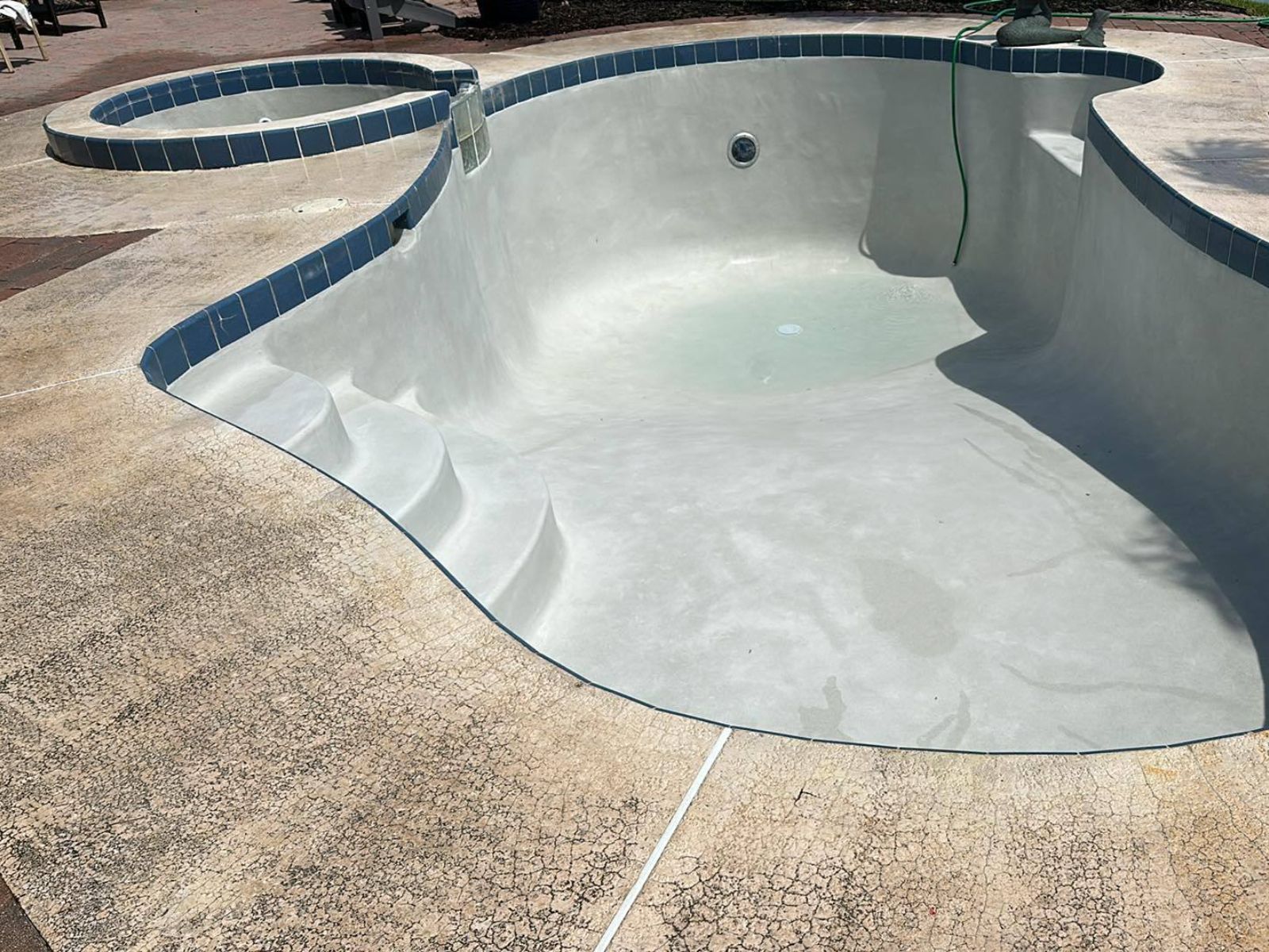 Empty concrete swimming pool with a smooth surface, surrounded by cracked concrete and a blue tiled edge.