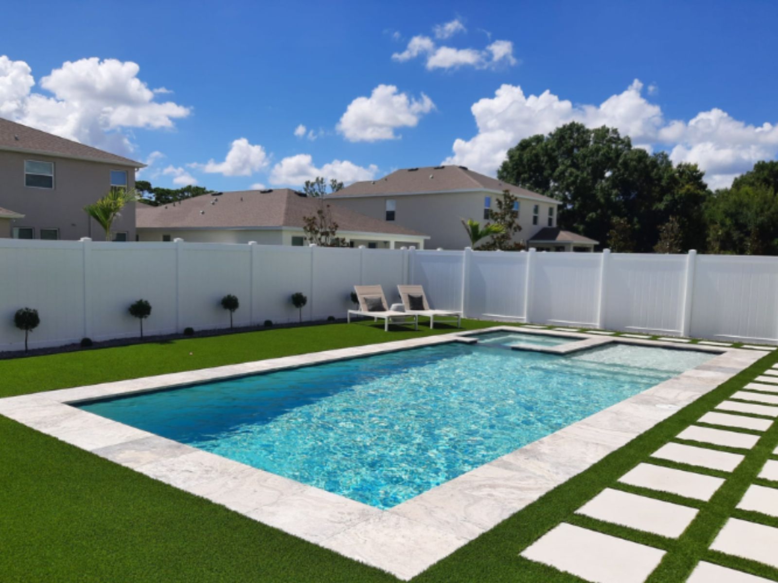 A bright outdoor patio featuring a pool, lounge chairs, and a tiki bar, surrounded by lush greenery and clear blue skies.