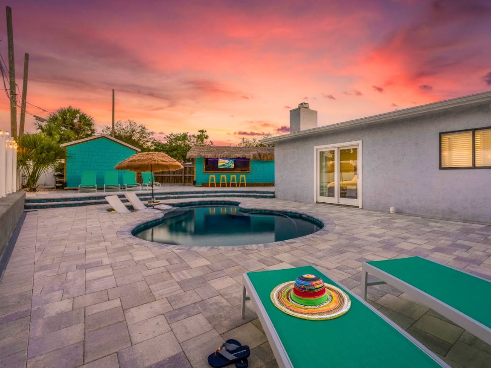 Vibrant sunset over a stylish pool area, featuring tropical decor and lounge chairs, creating a serene relaxation space.