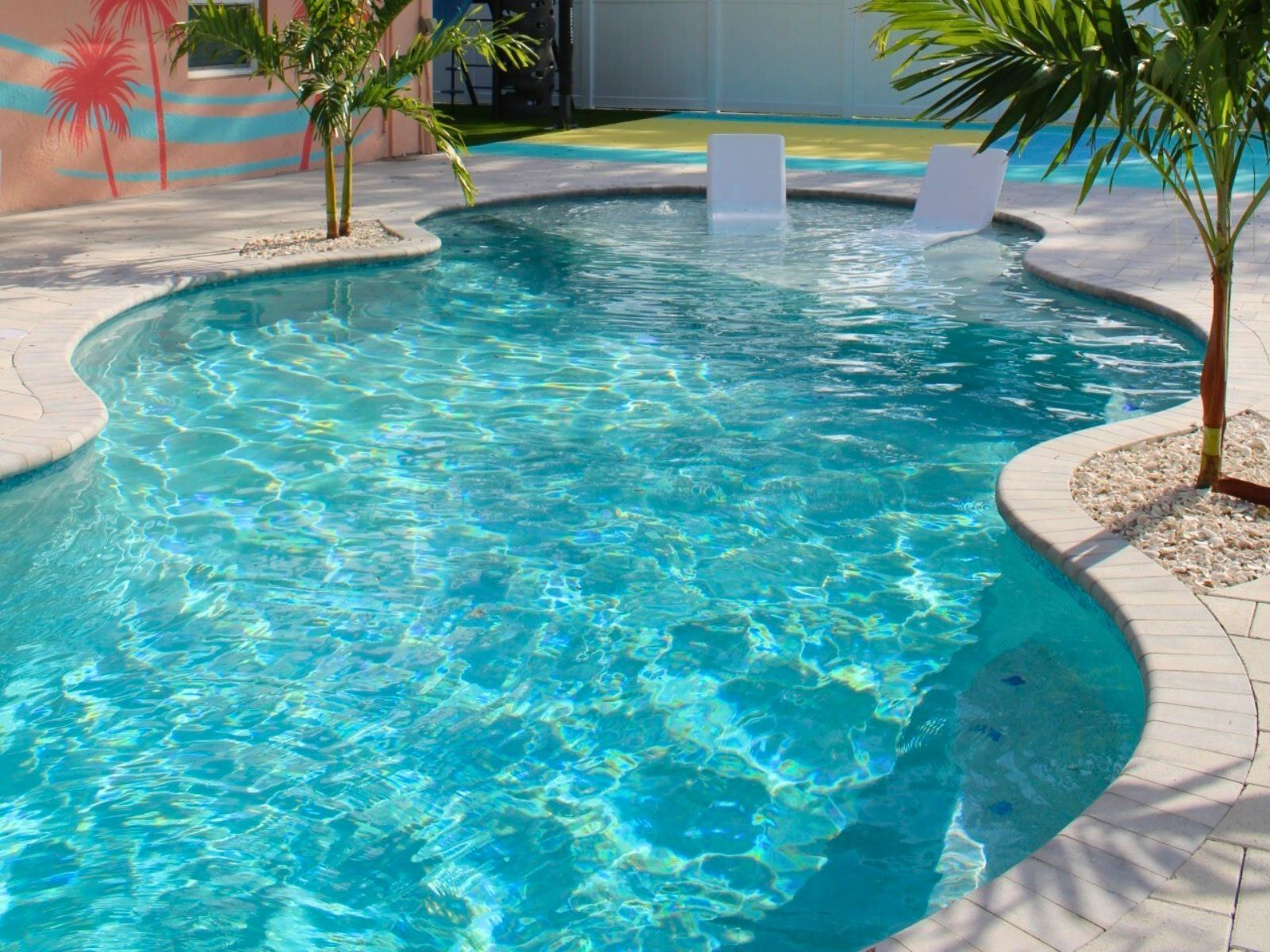 A serene pool surrounded by palm trees, featuring a curved edge and clear turquoise water, perfect for relaxation.