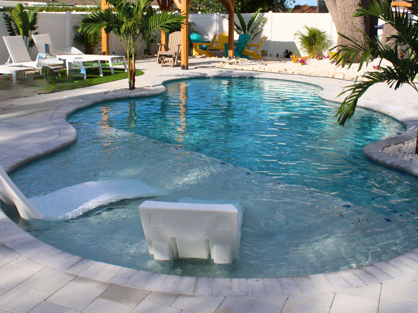 A sparkling blue pool surrounded by lush greenery, lounge chairs, and a playful slide, inviting relaxation and fun.