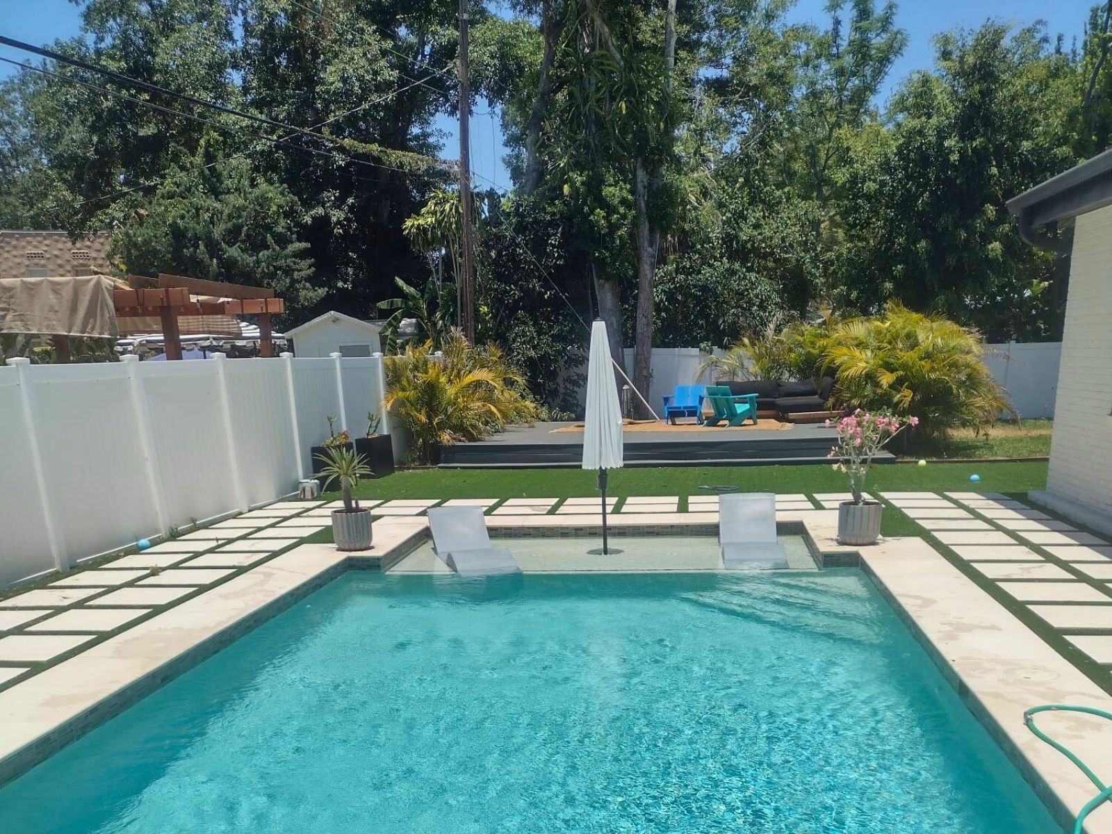Sunny backyard with a clear pool, lounge chairs, palm trees, and a cozy deck area ideal for relaxation and outdoor gatherings.