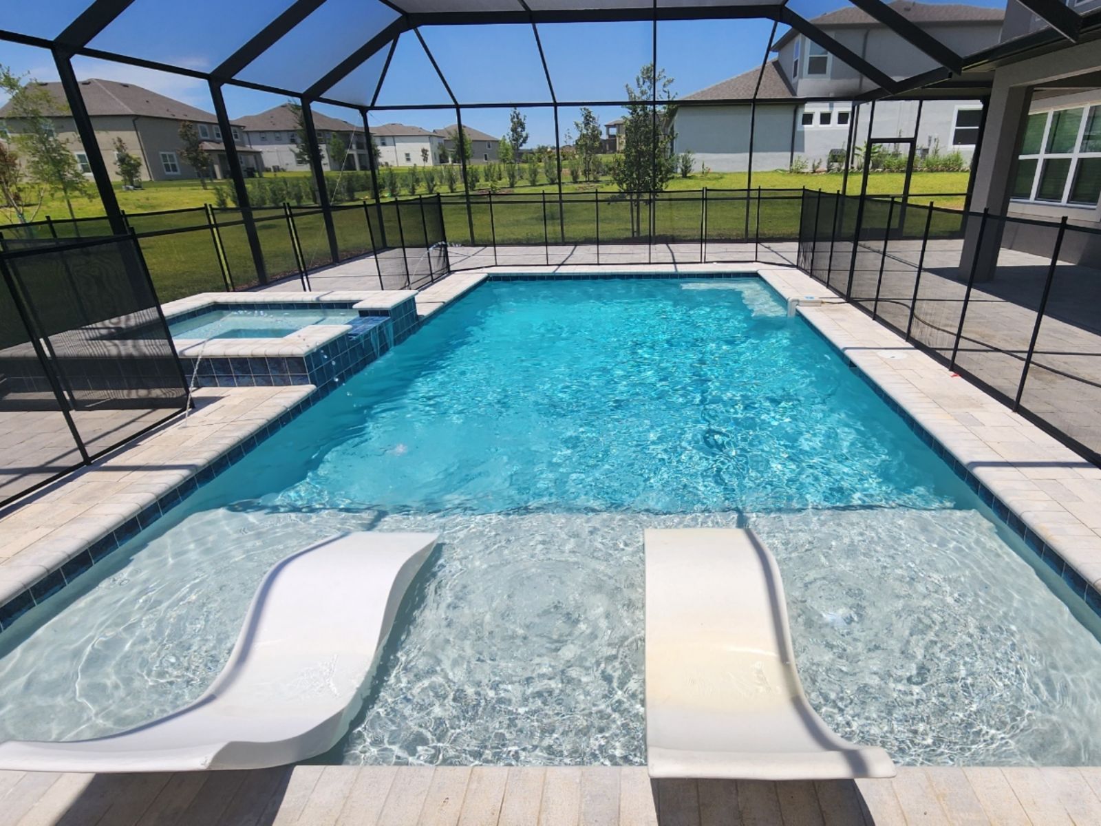 A sparkling blue pool with two white slides, surrounded by a protective screen and neatly landscaped backyard.