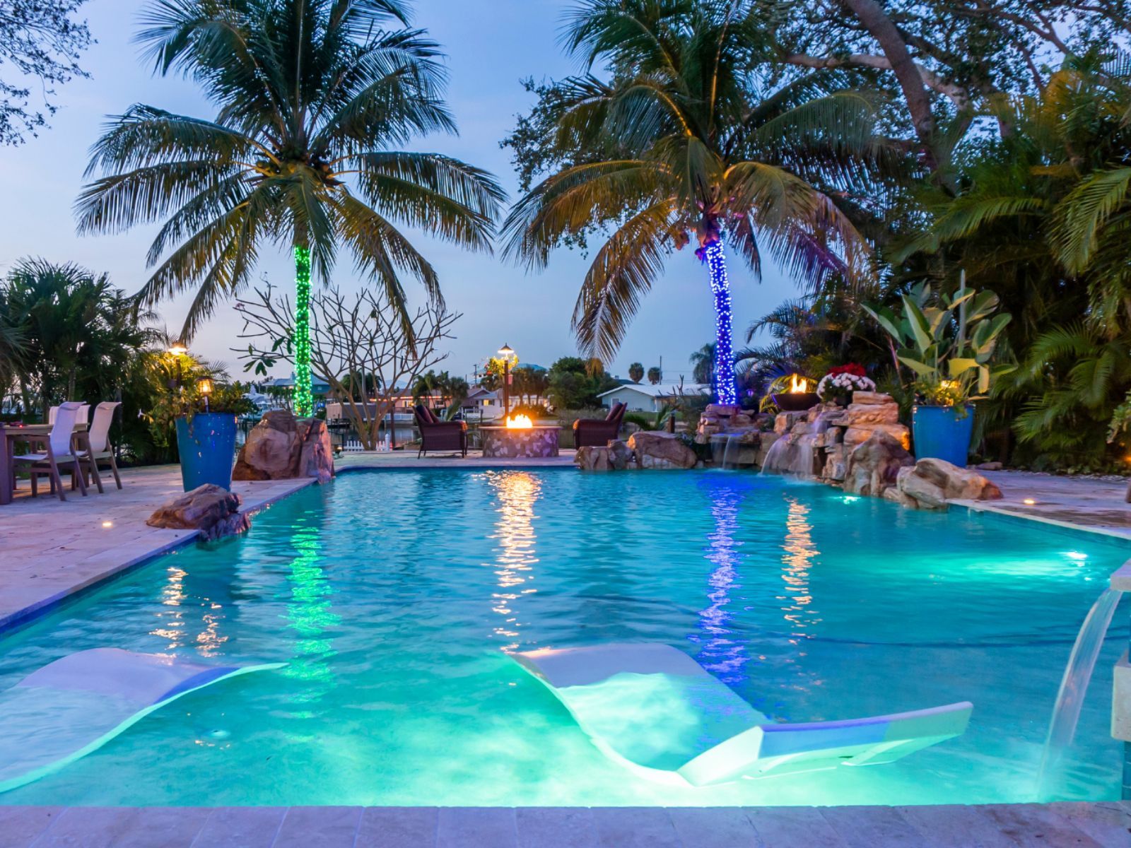 A serene pool area features illuminated palm trees, comfortable seating, and a tropical ambiance perfect for relaxation and entertainment.