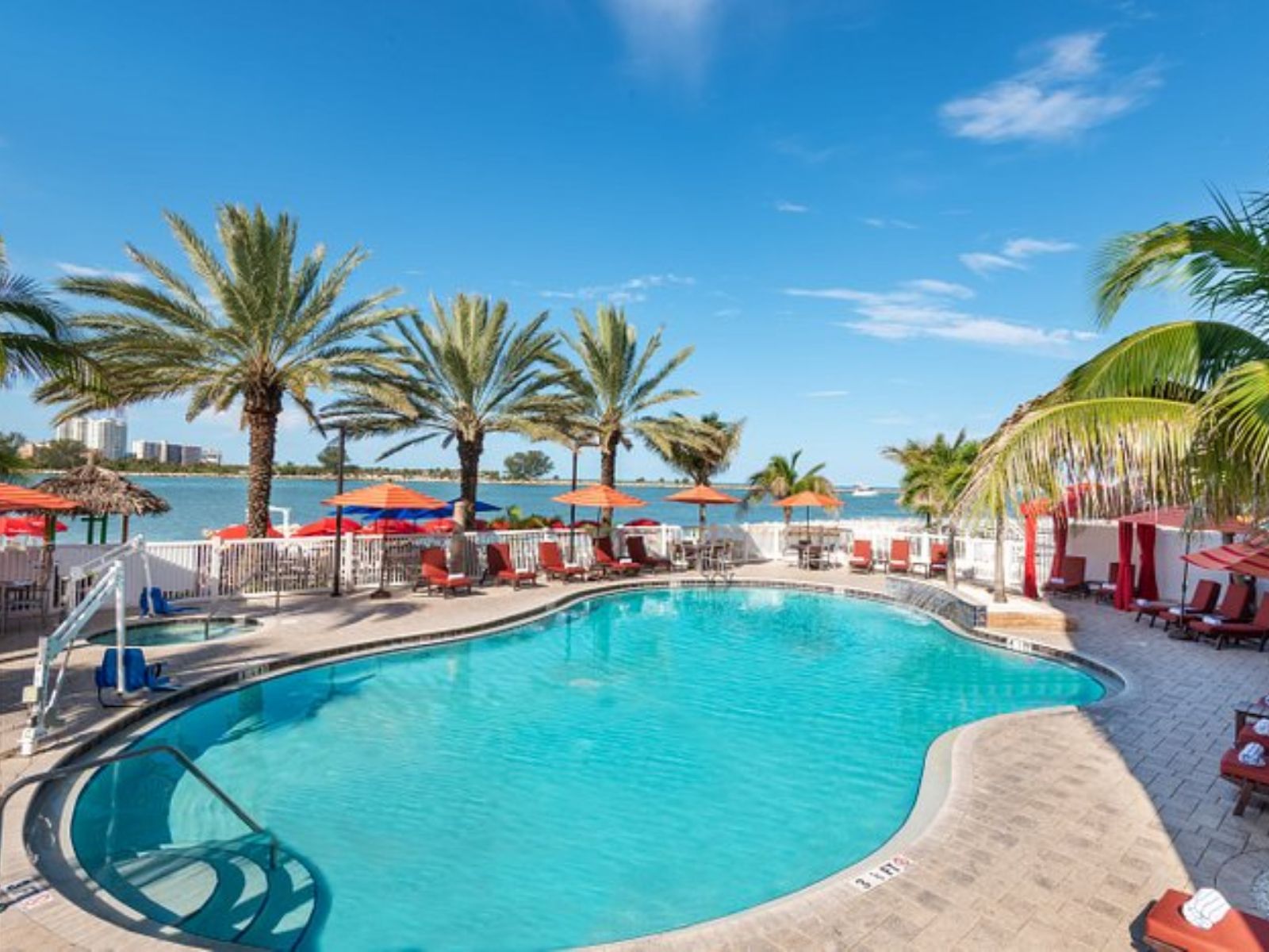 Waterfront resort pool surrounded by palm trees, lounge chairs, and scenic bay views