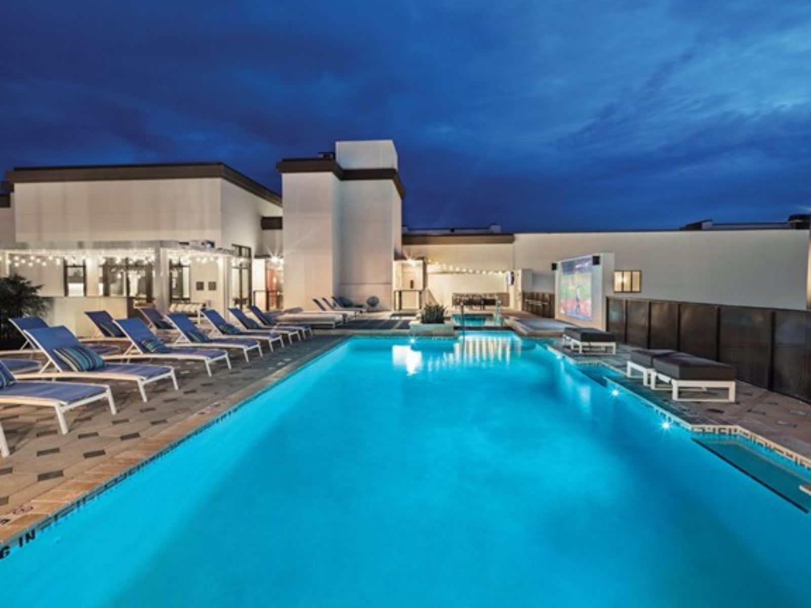 Rooftop swimming pool at night with lounge chairs, city views, and ambient lighting