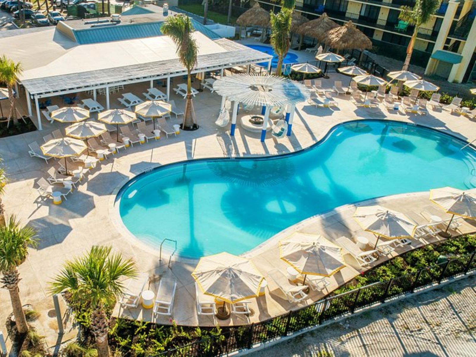 Aerial view of modern resort swimming pool with lounge chairs, umbrellas, and poolside bar area