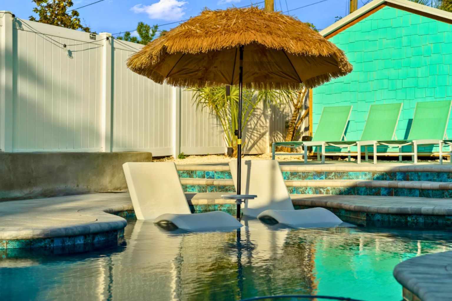 Shallow ledge commercial swimming pool with in-water lounge chairs and thatched umbrella, showcasing a clean, professionally maintained resort-style pool environment.