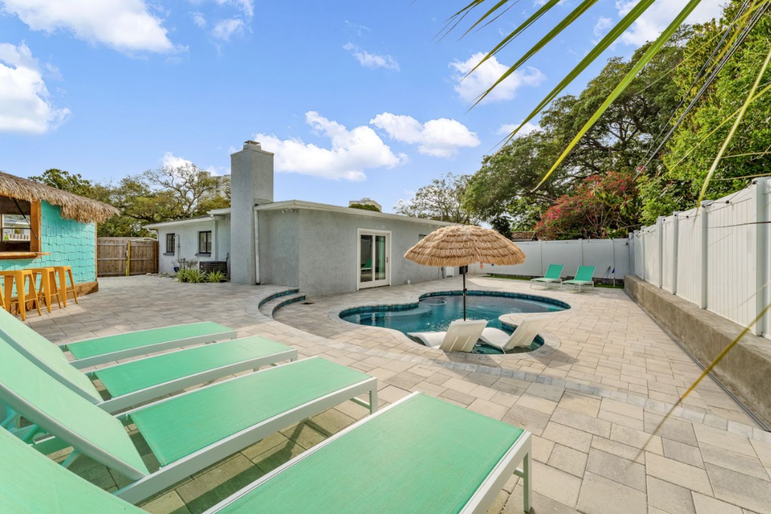 Commercial backyard pool with lounge chairs, thatched umbrella seating, and paved patio area, showcasing a professionally maintained outdoor residential pool environment and leisure space.