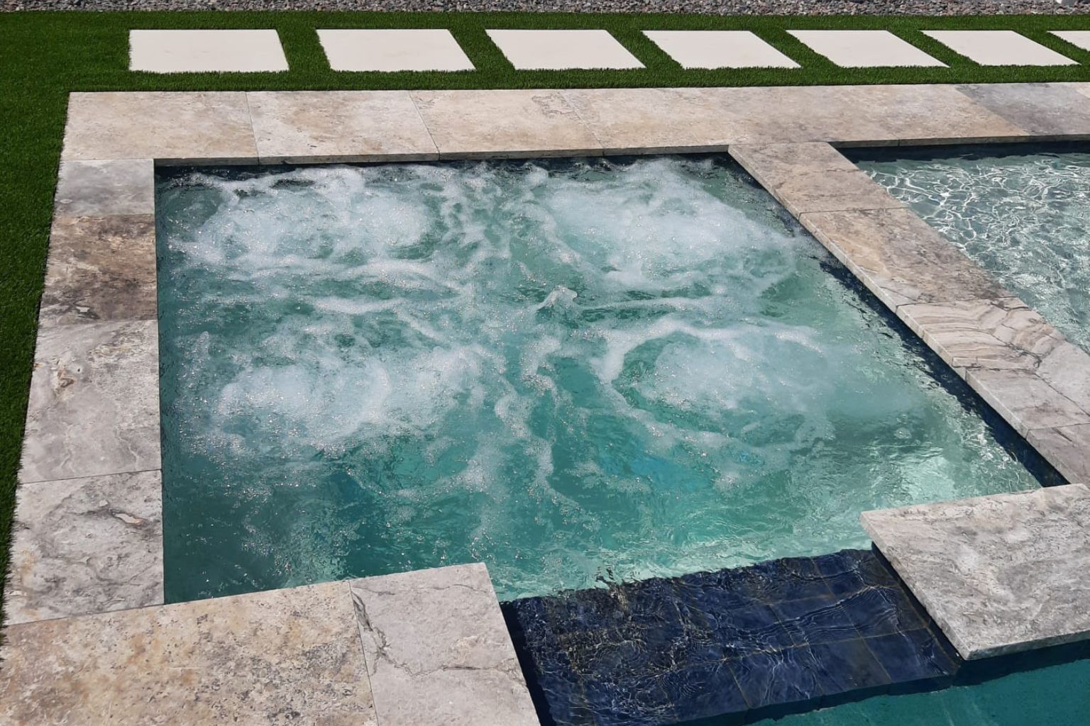 user-inserted Integrated spa and swimming pool with active jets creating bubbling water, natural stone coping, and modern backyard pool design with spillover spa feature.