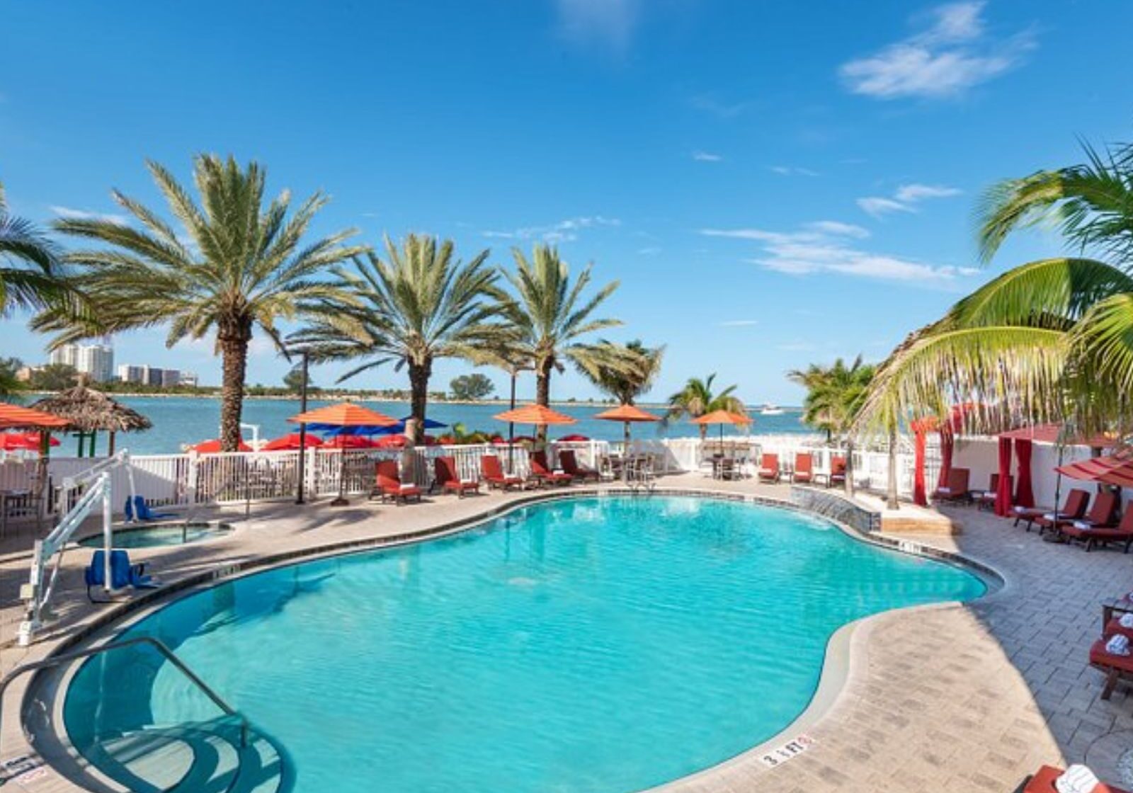 Waterfront resort pool surrounded by palm trees, lounge chairs, and scenic bay views